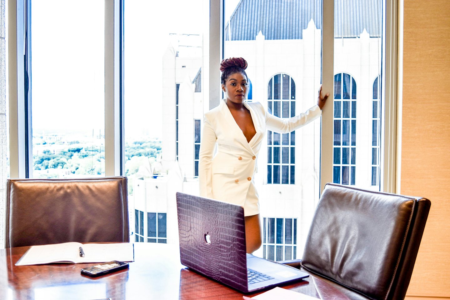 Young Black woman in white blazer dress in office meeting room.